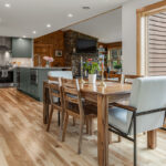 Green kitchen cabinets with island seating and light brown wood floors.