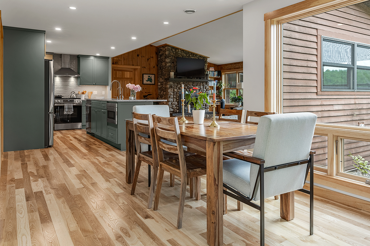 Green kitchen cabinets with island seating and light brown wood floors.