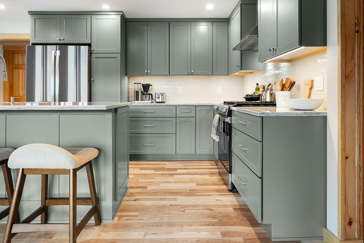 Green kitchen cabinets with island seating and light brown wood floors.