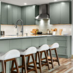 Green kitchen cabinets with island seating and light brown wood floors.