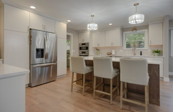 White painted kitchen cabinets with island seating and stainless steel fridge