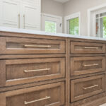 Beige painted kitchen perimeter cabinets with a 16-foot stained quartersawn white oak island wtih seating.