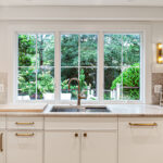 White painted kitchen cabinets with sink view out of a large window.