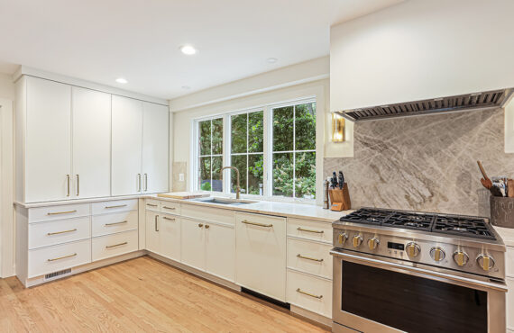 White painted kitchen cabinets with sink view out of a large window. Shows professional stainless steel stove.