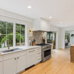 White painted kitchen cabinets with sink view out of a large window. Shows professional stainless steel stove.