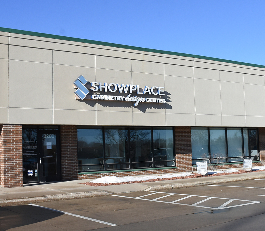 Shows the external building of Showplace Cabinetry Design Center Des Moines Showroom. It is a beige building with bricks around the windows and doorway.