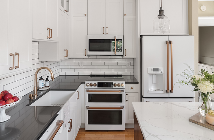 Showplace designed kitchen with white inset cabinets with gold handles, black countertops, and a white subway tile backsplash.