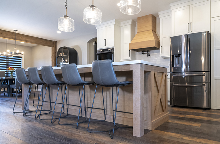 Natural stained wood island in a kitchen with white inset cabinets that have black handles. This kitchen was designed by Showplace Design Center.