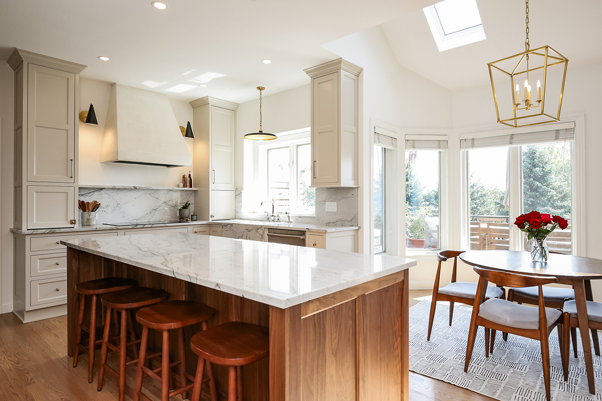 We see the same dual tone kitchen with stained wood and white cabinets from another angel. We can see the kitchen has a lot of natural lighting that makes the wood stain appear lighter.