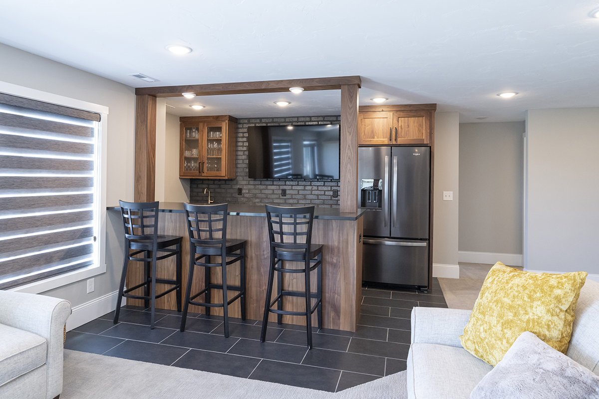 Basement bar with an exposed brick backsplash. A large TV is over the bar.