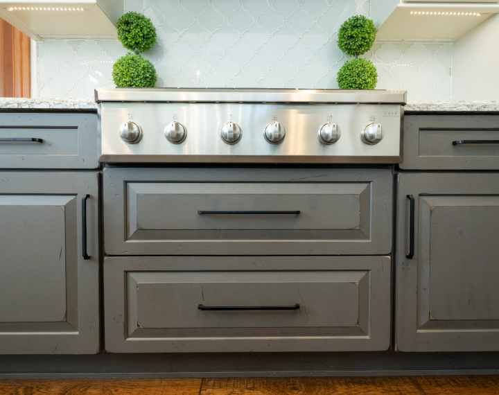 Denver kitchen design that features a stainless steel cooktop stove and dark grey cabinets. The backsplash is white and the handles to the cabinets are brushed black.