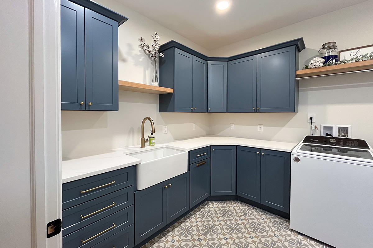 Blue painted laundry room cabinets with white appliances and stained floating shelves