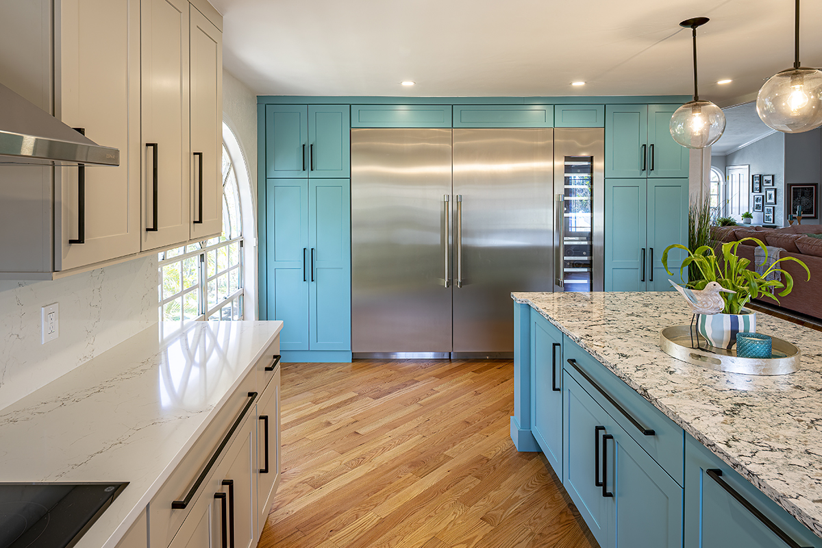 Dual tone kitchen with teal blue cabinets and marble counter tops. Half of the kitchen is teal blue, the other half of the kitchen is beige. The black handles remain consistent throughout.